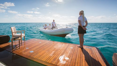 Une stewardess sur la plateforme de bain d'un yacht accueille les charter guests arrivant par annexe