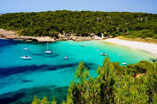 La plage de Cala Trebaluger avec ses eaux turquoises, sa vgtation luxuriante et quelques bateaux au mouillage