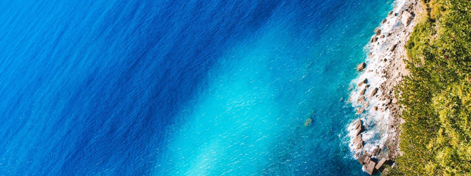 Vue aérienne de la mer avec des eaux turquoises, une plage de galets et une végétation verte