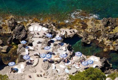 Le restaurant de plage La Fontelina  Capri avec des parasols bleus et blancs, des eaux turquoises et des gens qui se baignent