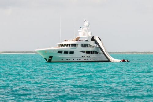 Un yacht  moteur de luxe  l'ancre avec un toboggan aquatique qui part du haut du bateau et qui arrive dans la mer