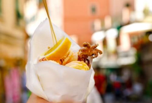 Une femme tenant un cornet de fruits de mer frits dans le village de Riomaggiore