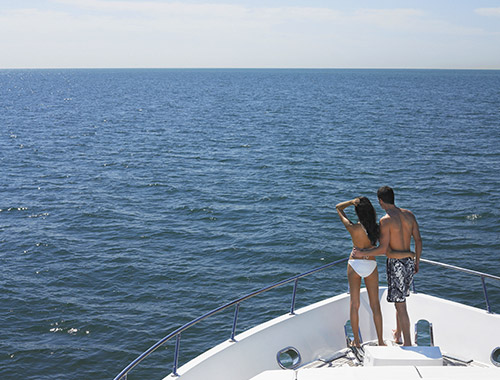 Un couple en maillot de bain se tenant à la proue d'un yacht de location lors de leur croisière d'été en Méditerranée