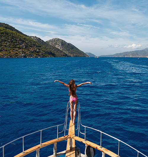 Une femme en maillot de bain se tenant à la proue d'un yacht de location en Méditerranée