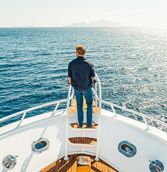 Un propritaire de yacht  la proue de son bateau contemplant l'horizon